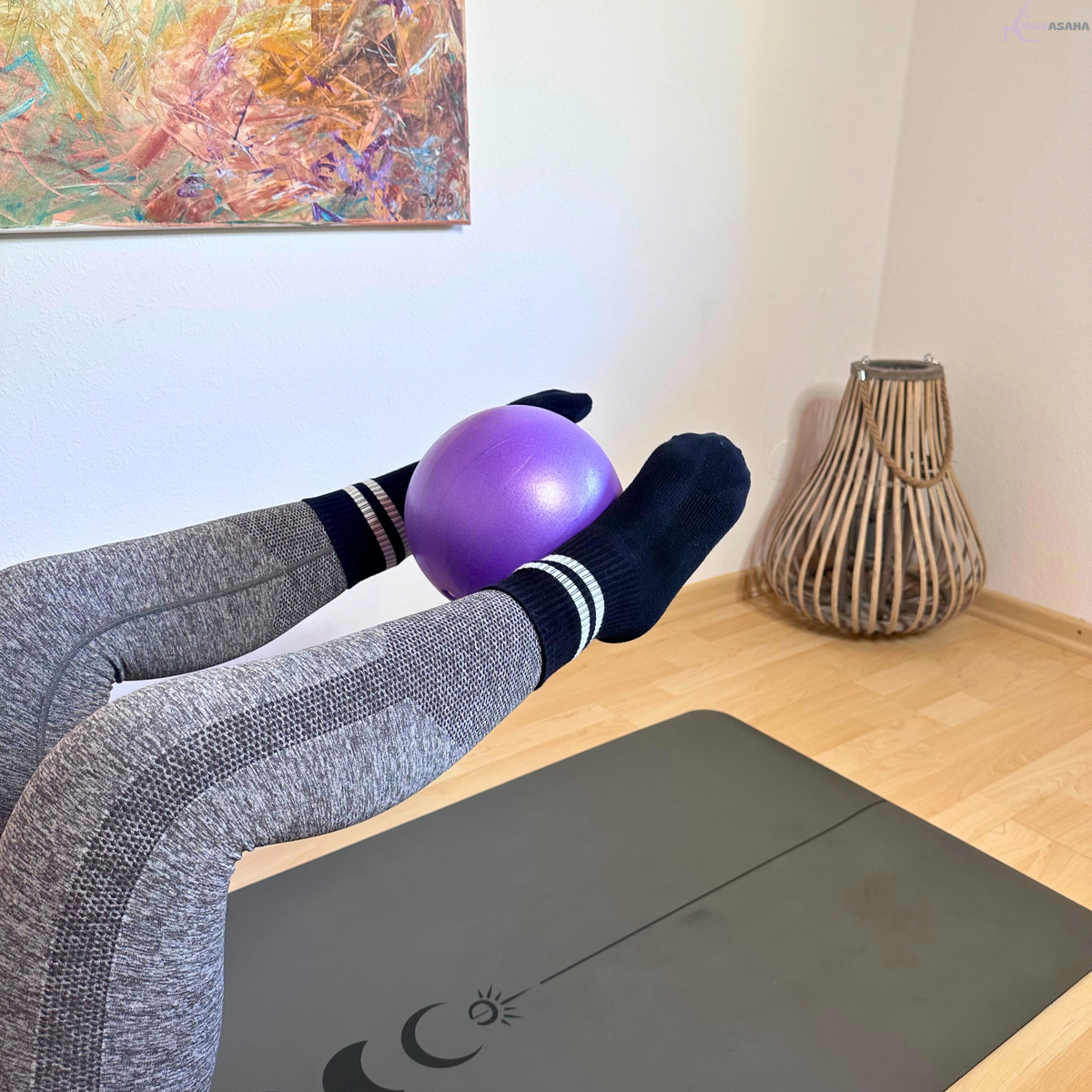 Gymnastikball des Movasana Pilates Set zwischen den Knöcheln bei angehobenen Beinen
