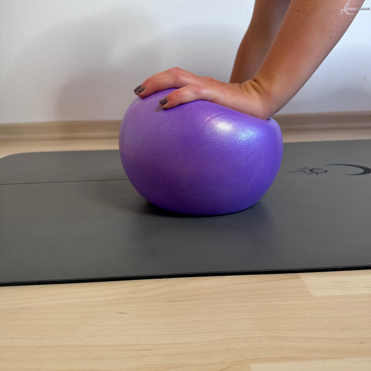 Hand drückt den lila Gymnastikball des Movasana Pilates Set auf der Matte ein