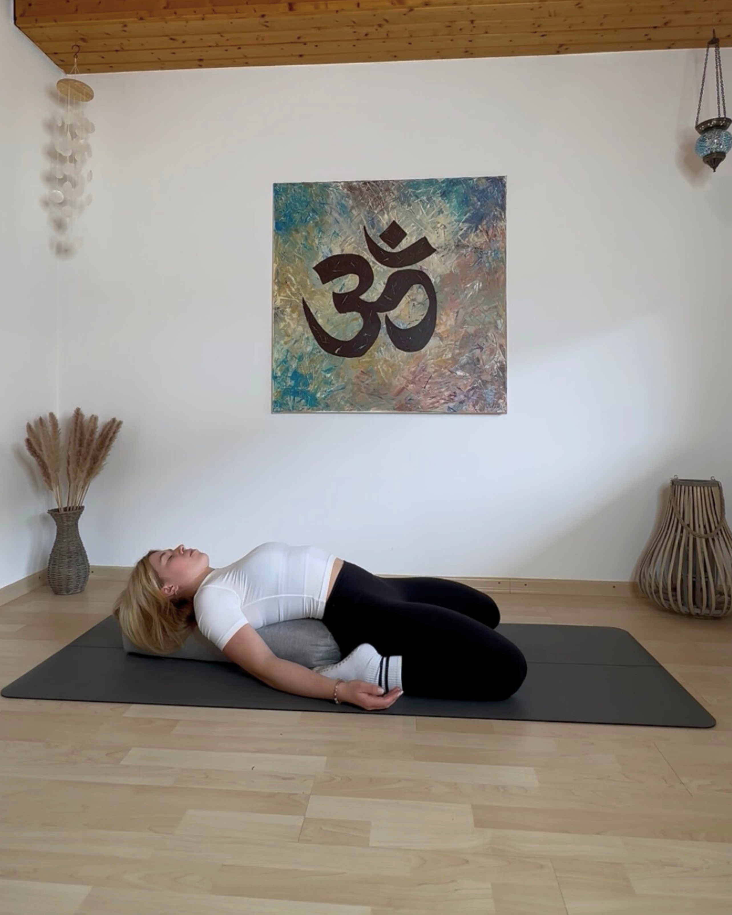 Frau liegt rücklings über dem Yoga-Bolster, die Knie angewinkelt
